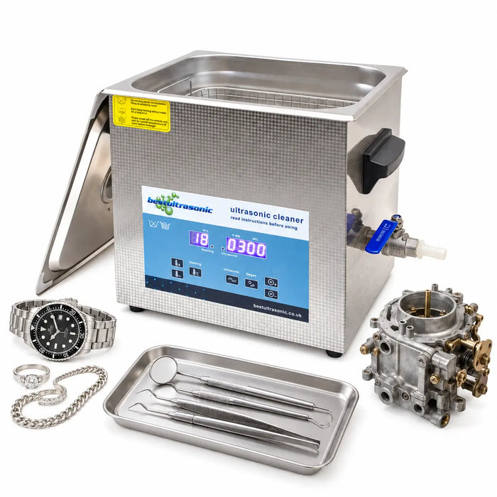 A stainless steel ultrasonic cleaner kit shown on a white background, with the lid open to reveal the interior basket, a blue control panel, a metal tray holding dental tools, a watch, rings, and a carburetor beside it.